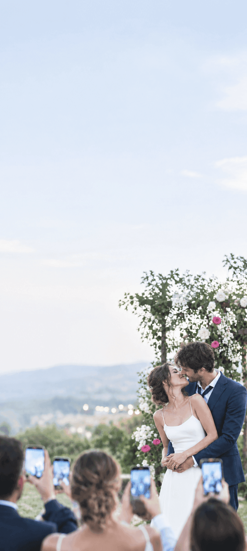 Sposi che si baciano durante la cerimonia, circondati da invitati che fotografano il momento con lo smartphone
