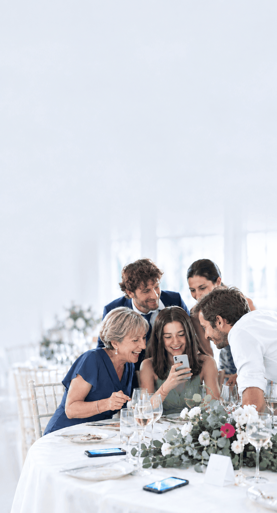 Invitati al tavolo del ricevimento che guardano ridendo una foto sullo smartphone