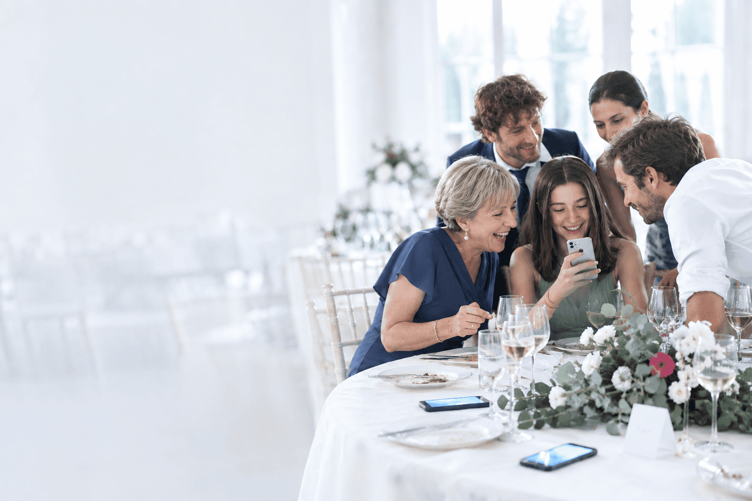 Invitati al tavolo del ricevimento che guardano ridendo una foto sullo smartphone